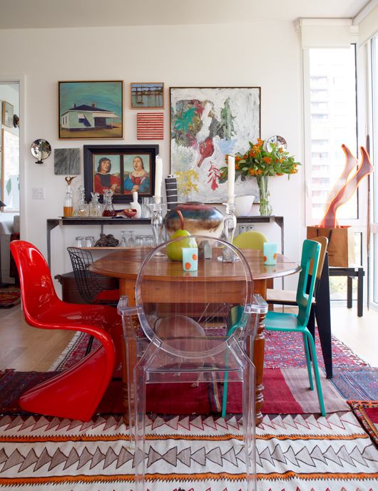 a bright dining room with some bold rugs, a colorful gallery wall, a stained table and mismatching chairs plus some more decor