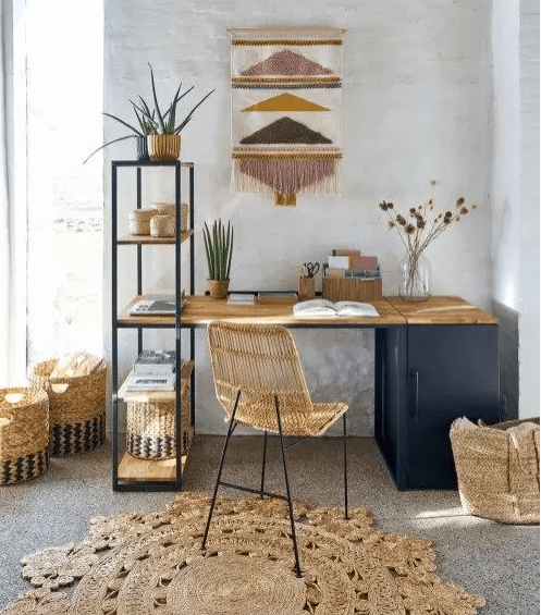 a bright home office with a navy desk, a rattan chair, a jute rug, baskets, a bright wall hanging and an open shelf