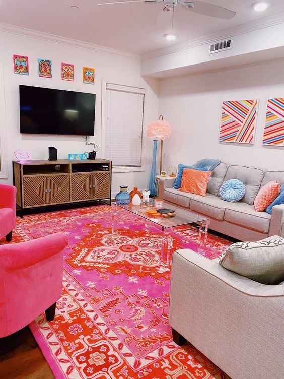 a bright living room with neutral seating furniture, a pink and red rug, pink chairs, some colorful artwork and a glass coffee table
