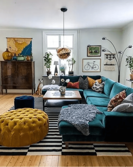 A bright mid century modern living room with a stained storage unit, a dark green sectional, a yellow ottoman and a navy pouf, colorful pillows and a bold gallery wall