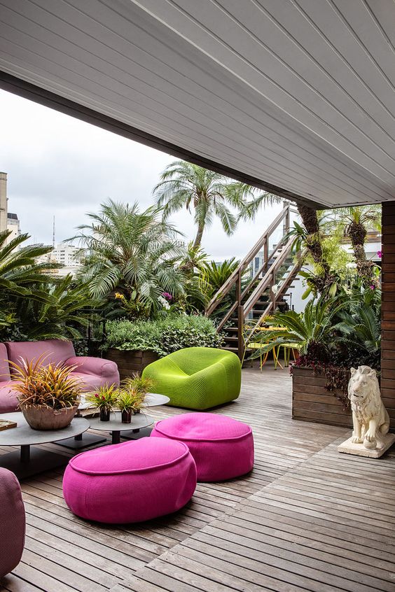 a bright modern terrace with a pink sofa and hot pink poufs, a green chair and some laconic decor