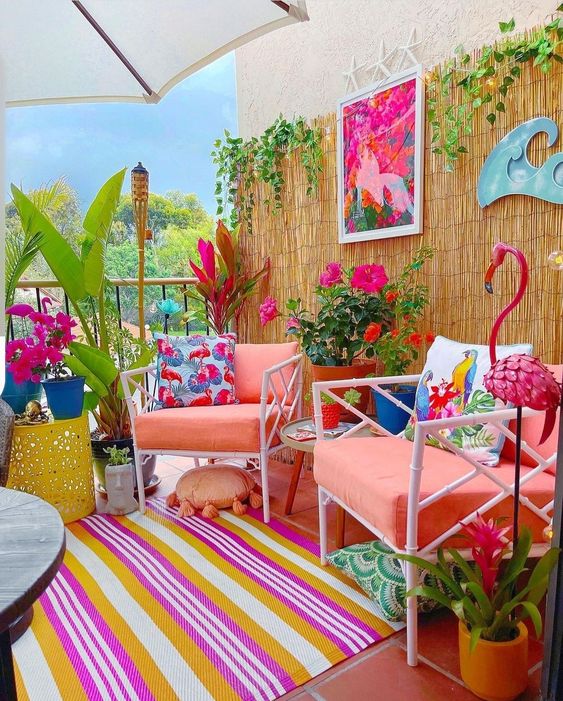 a bright terrace with coral chairs, a colorful striped rug, bold pillows, potted plants and blooms and colorful decor