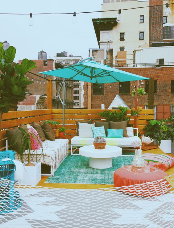 a bright terrace with white sofas, colorful pillows, a coral pouf and some pillows, a turquoise umbrella and a hamoock