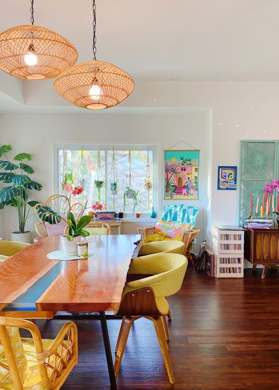 a bright tropical dining room with living edge table, yellow chairs, pendant lamps, potted plants and colorful posters