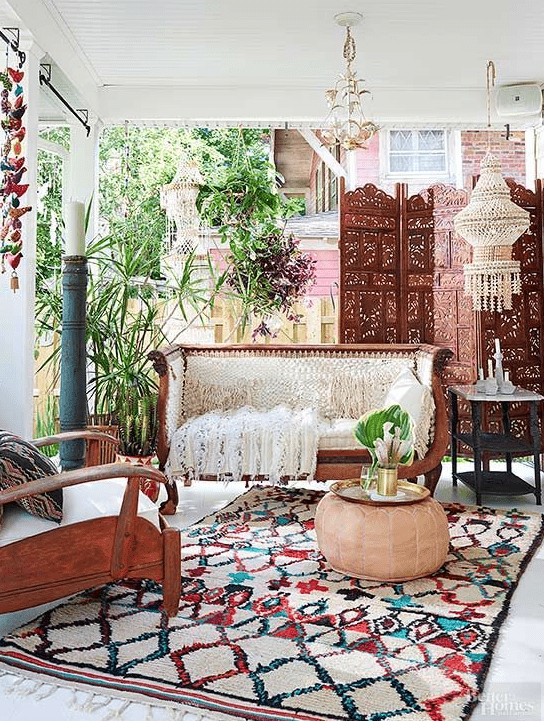 a chic boho porch with a wood carved bench, a chair, a printed rug, lanterns and a carved wooden screen