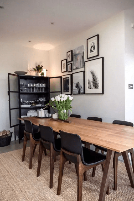 a chic modern dining room with a black storage unit and chairs, a stained coffee table, a gallery wall, a jute rug and some blooms