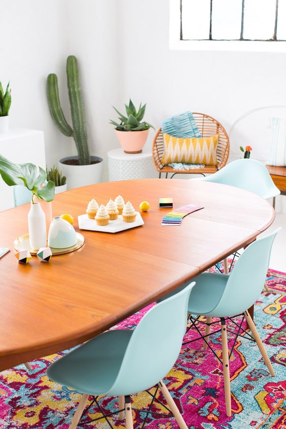 a colorful boho dining room with a bright rug, pillows and aqua chairs, potted succulents and cacti is amazing