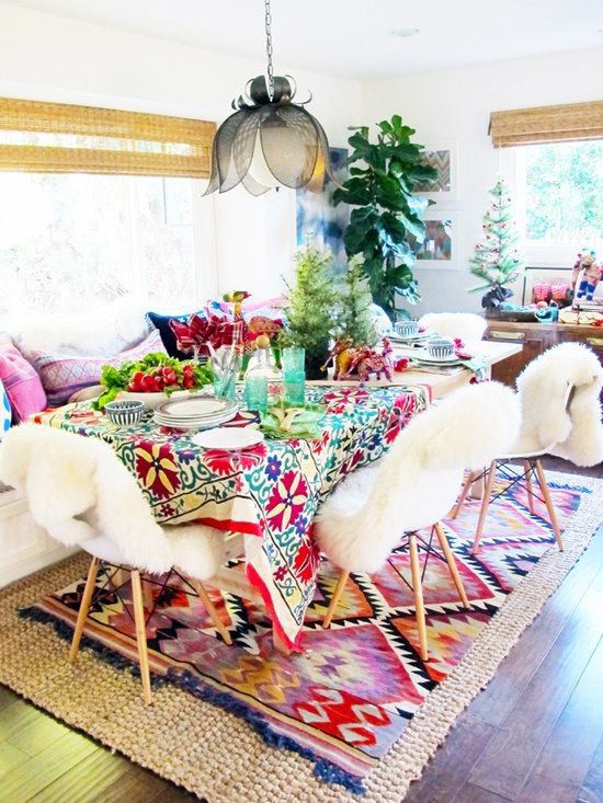 a colorful boho dining space with a white sofa and colorful pillows, a bold rug, bold linens and white chairs with faux fur