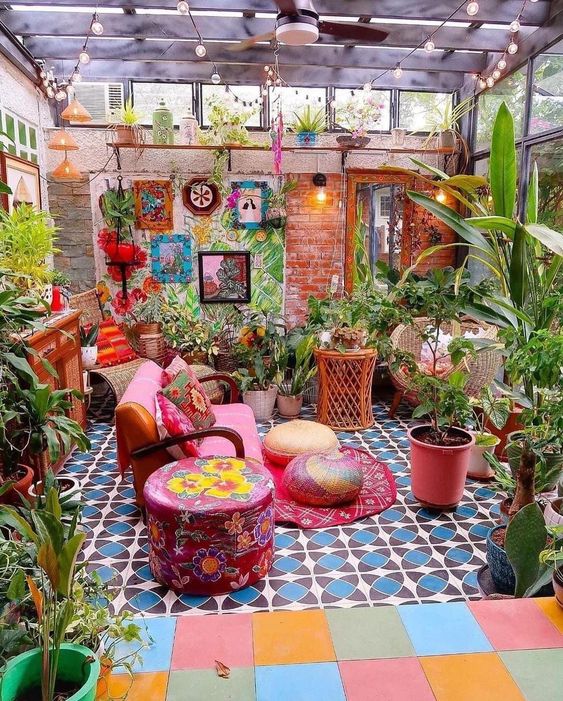 a colorful boho terrace with a pink sofa, colorful tiles, a bold accent wall, artwork, potted plants and blooms is very fun