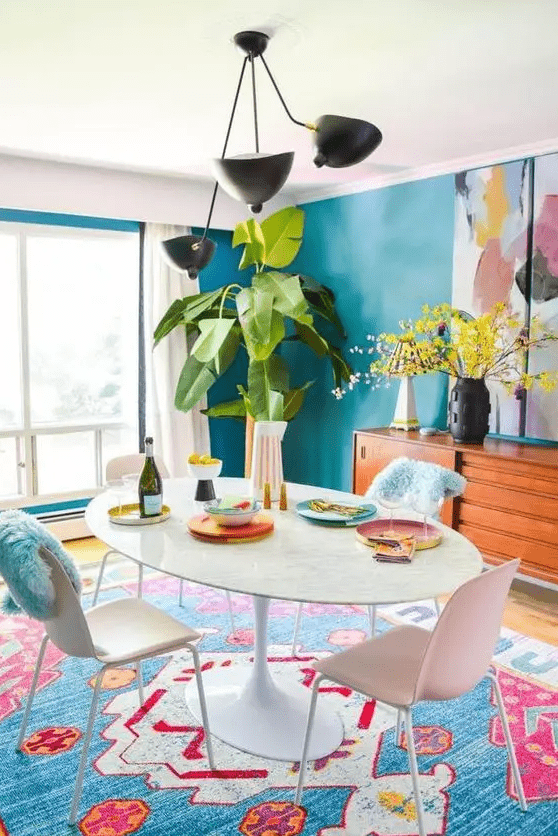 a colorful dining with blue walls, a colorful rug, a white table and chairs, greenery and a bold artwork