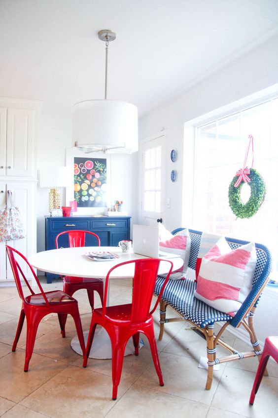 a colorful dining zone with a navy credenza, a table, a blue rattan bench, red chairs and colorful decor