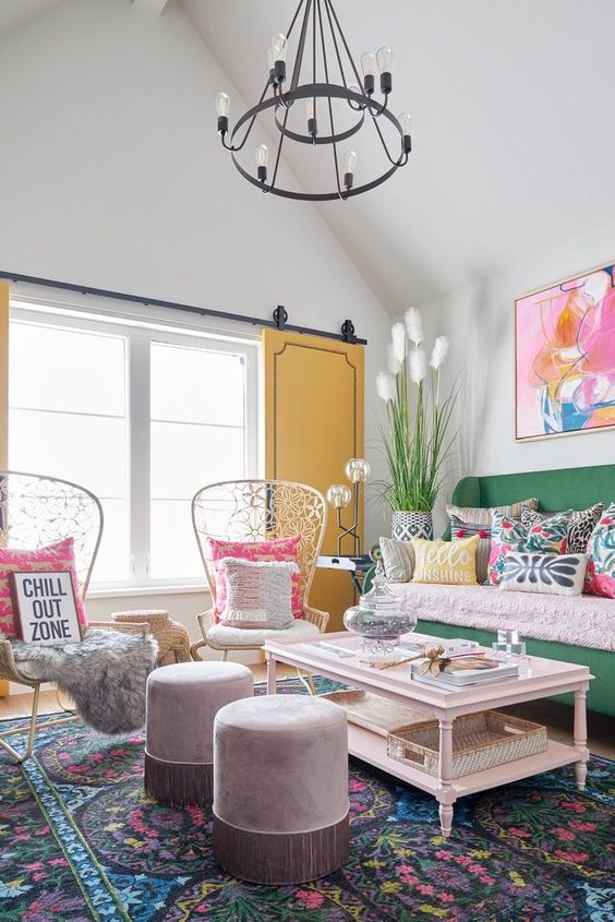 a colorful living room with a bold rug, a green sofa with pillows, papasan chairs, a coffee table, poufs and some bold wall art