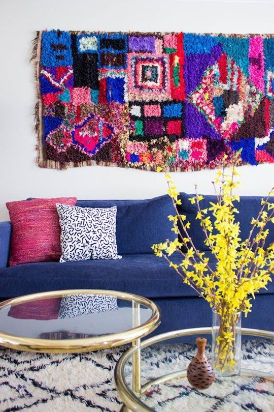 a colorful living room with a navy sofa and colorful pillows, a bright boho rug, glass coffee tables and a printed rug