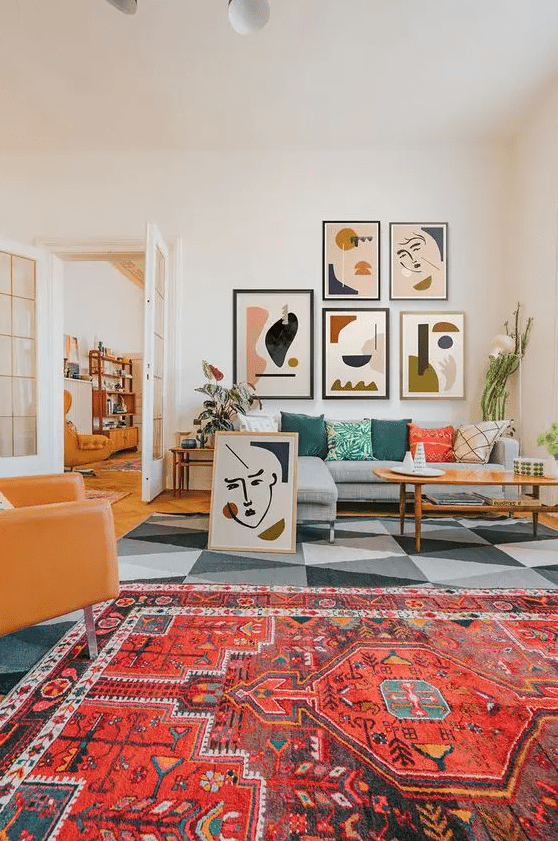 a colorful modern living room with a bold boho and geometric rug, a grey sofa with pillows, a modern gallery wall and an amber leather chair