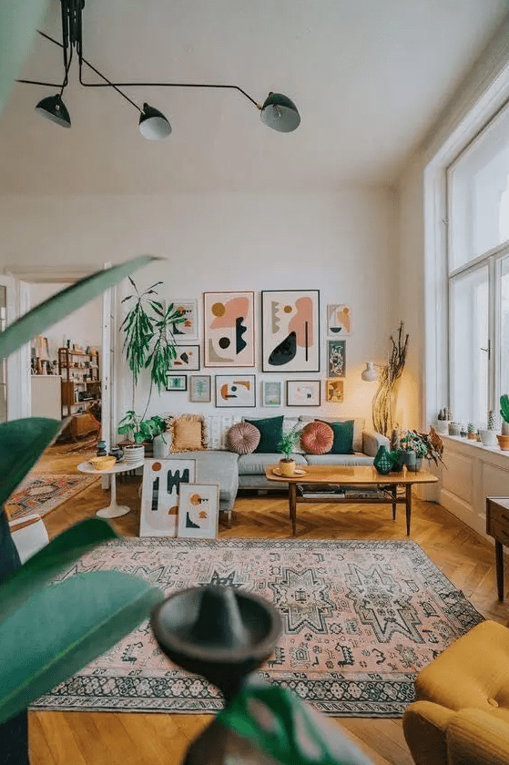 a colorful modern living room with a grey sofa and colored pillows, a printed boho rug, a coffee table, a bright gallery wall and lots of potted plants