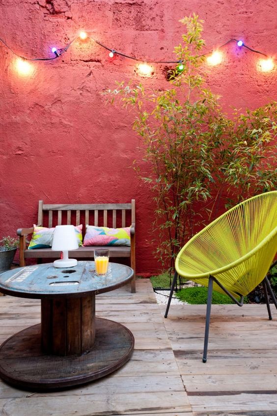 a colorful space with red walls, a neon yellow chair, a spool coffee table, colorful pillows and rugs and greenery
