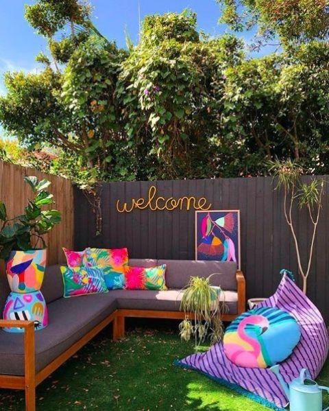 a colorful terrace with a green lawn, a grey sectional, colorful pillows, a bright beanbag chair with a pillow and some greenery