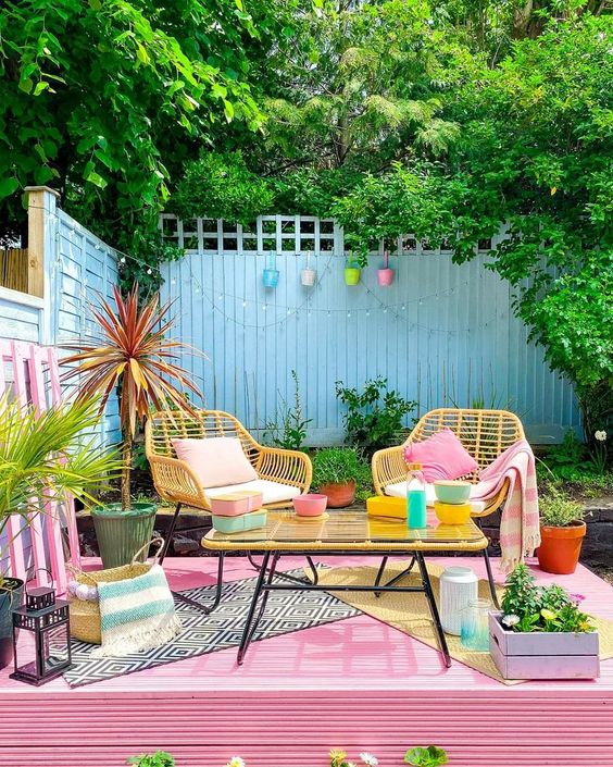 A colorful terrace with a pink deck, yellow chairs and a table, bright accessories and decor is really dopamine infusing