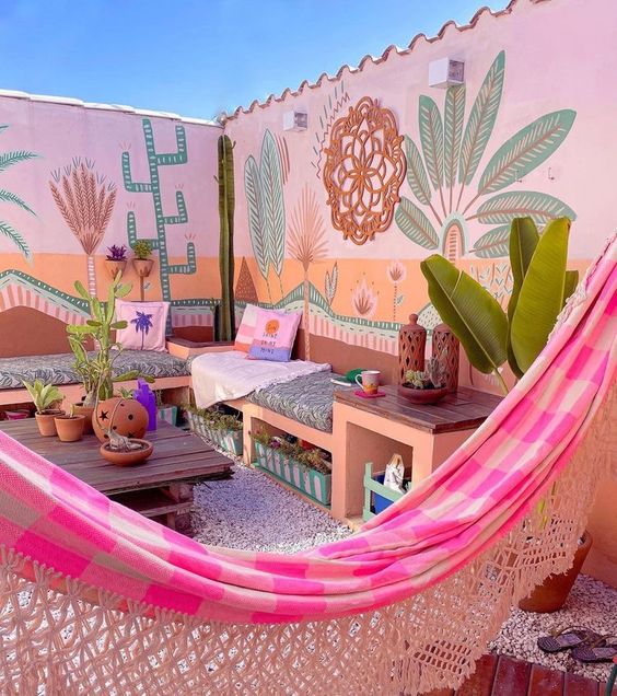 A colorful terrace with bright walls, a built in sofa with bright pillows, a pink hammock, potted plants and some lovely decor