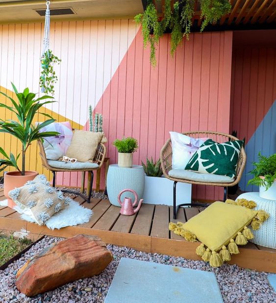 a colorful terrace with rattan chairs, colorful and printed pillows, a bold geometric wall and potted plants