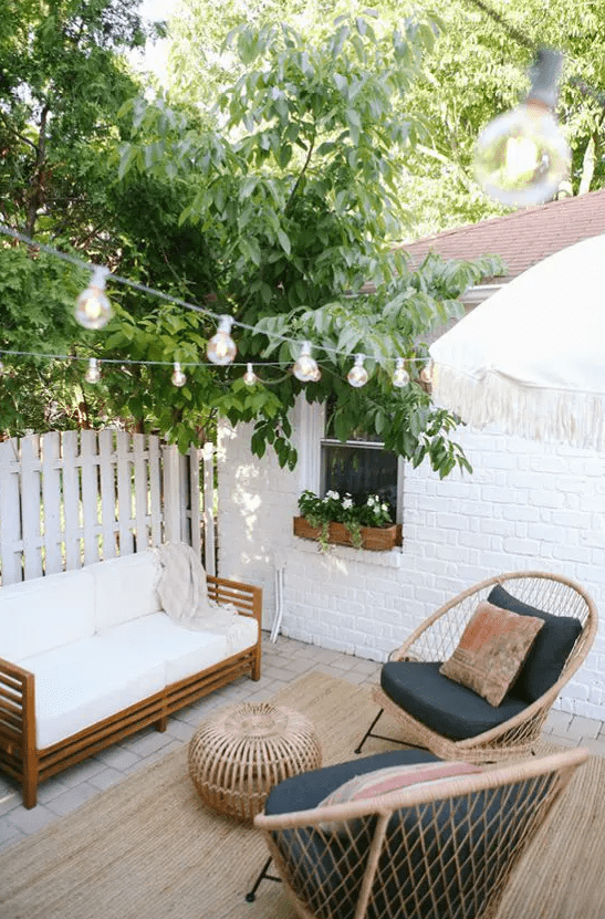 a cool outdoor nook with rattan furniture, a rattan pouf, string lights and lots of greenery around is a lovely space