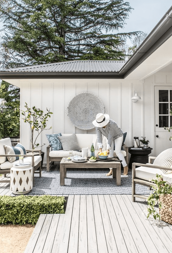 a cozy Scandinavian terrace with simple wooden furniture, white upholstery, a lemon tree and striped pillows