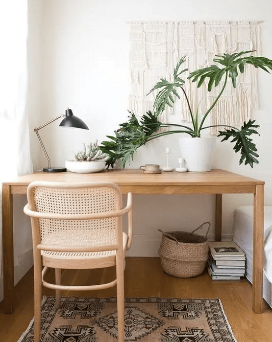 a cozy boho home office nook with a sleek desk, a rattan chair, a boho rug, a basket and a macrame hanging plus potted plants