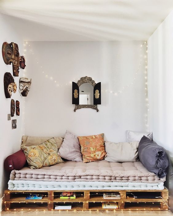 a cozy nook with a pallet sofa and pillows, some lights and books inside, with a mask gallery wall and a mirror is amazing