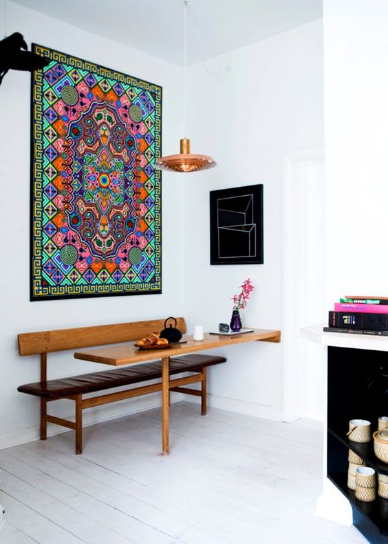 a creative space with a bold boho rug on the wall, a built-in mini table and a bench, a pendant lamp and some decor