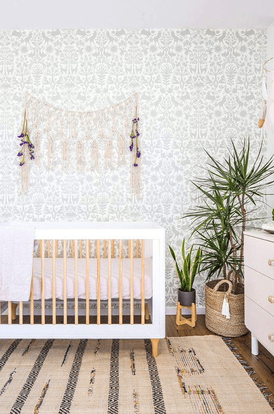 a cute boho nursery with a botanical wallpaper wall, a boho rug, a crib, macrame and potted greenery