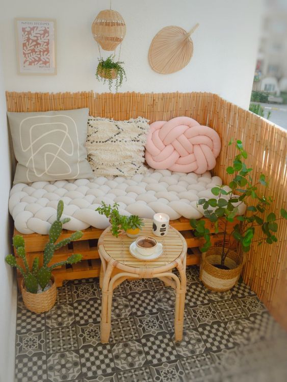a cute little balcony with a pallet sofa and pillows, a stool, potted plants and some boho decor is great