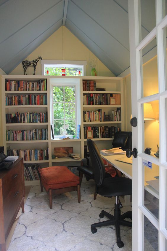 a cute shed home office with bookshelves, a white desk with black chairs, a storage cabinet and some decor
