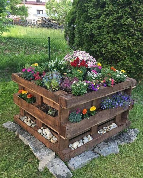 a dark-stained pallet garden with greenery and blooms is a cool and bold alternative to a raised garden bed, with pebbles and rocks around