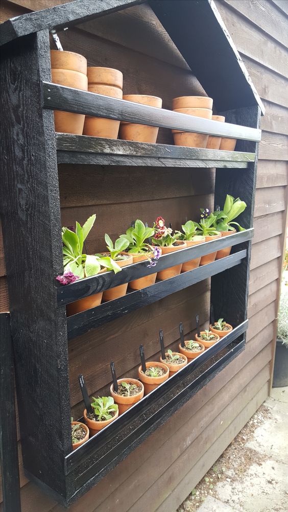 a dark-stained pallet house-shaped shelf with planters and various blooms and succulents is a creative idea for a rustic space