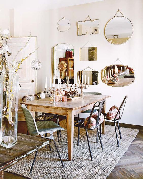 a dining space with a mirror gallery wall, a stained table, mismatching chairs, some decor and a jute rug