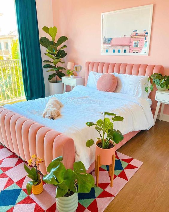 a dopamine decor bedroom with a pink upholstered bed, neutral bedding, a bold geo rug, pink walls and teal curtains