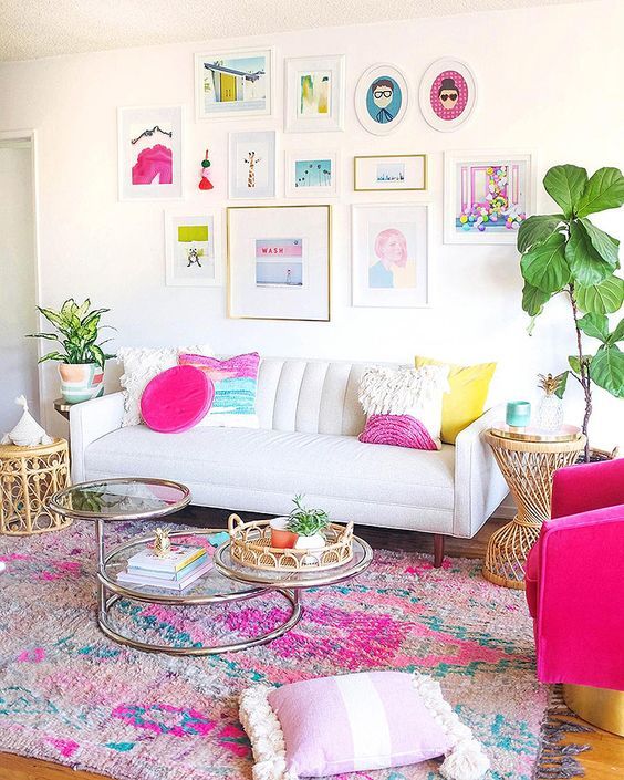 a dopamine decor living room with a colorful rug, a white sofa with bright pillows and a bright gallery wall, a hot pink chair and some rattan furniture