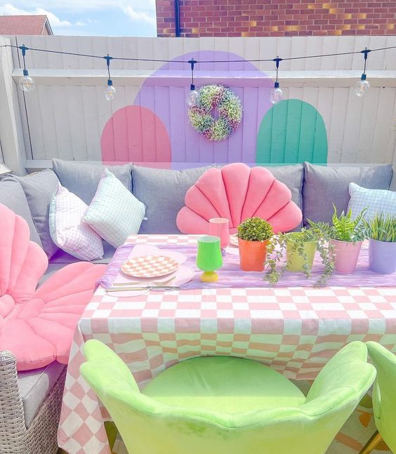a dopamine terrace with a lilac sofa and pink and blue pillows, green chairs, and a colorful wall and some potted plants
