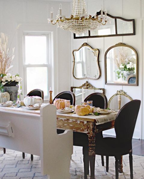 a farmhouse dining room with a mirror gallery wall, a shabby chic table, black chairs and a white bench and a crystal chandelier