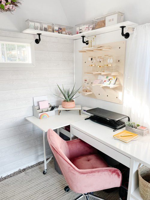 a farmhouse home office with white planked walls, a white desk, a  pink chair, a memo board and a shelf and some lovely decor
