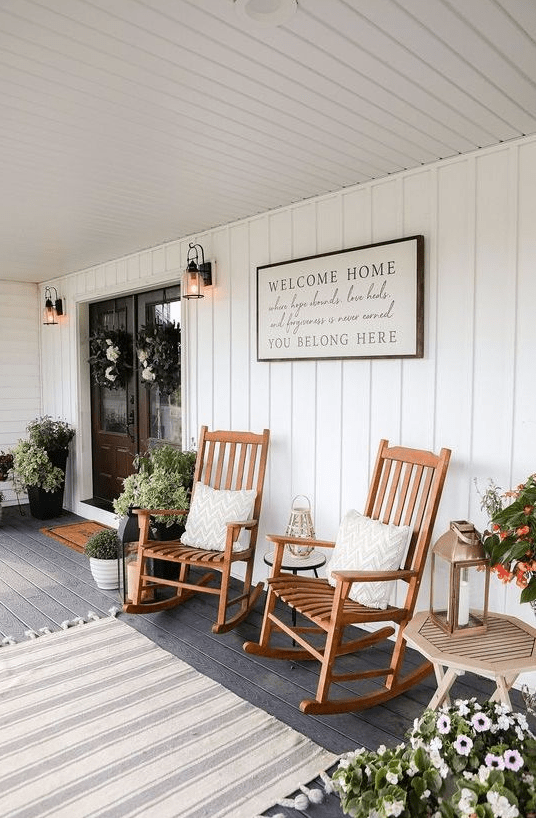a farmhouse porch styled for summer, with wooden rockers, potted plants, a sign and a rug is a very welcoming and cool space