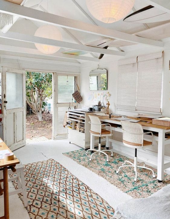 a farmhouse shed home office with a double desk, woven chairs, printed rugs and some more tables and stools for crafting