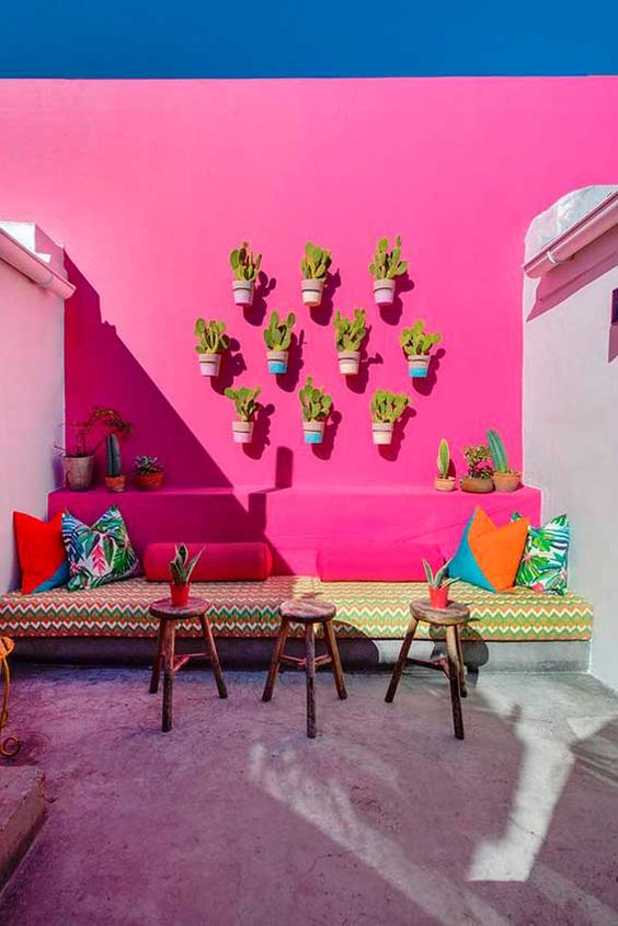 a hot pink terrace with a built-in sofa and wall-mounted planters with cacti, colorful pillows and stools