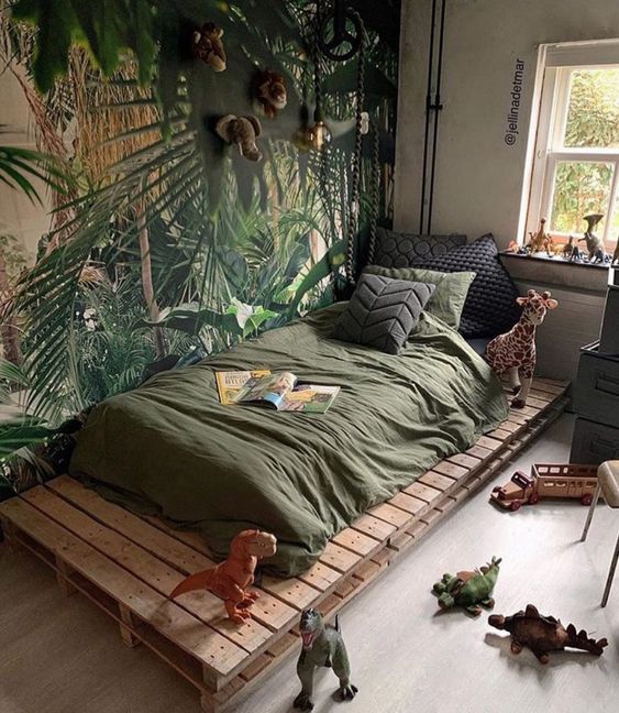 a kids' room with a bold jungle accent wallw ith faux taxidermy, a pallet bed with green bedding and some toys