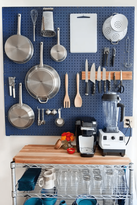 a kitchen done with a navy pegboard used for storing cookware and knives, which is a smart solution