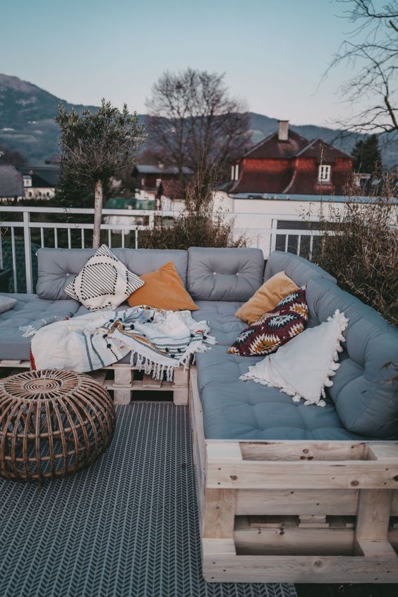 a large pallet sofa with colorful pillows, a rattan table are cool pieces for outdoors, they will match many terraces