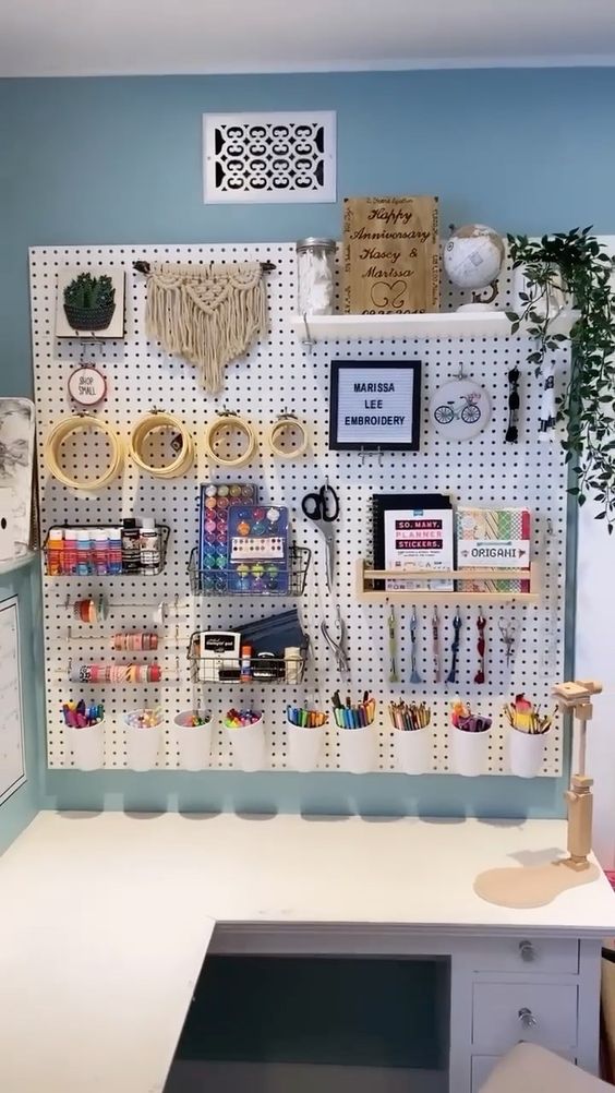 a large white pegboard organizing the craft space, with shelves, glasses and hooks, is a perfect idea for a craft room or studio