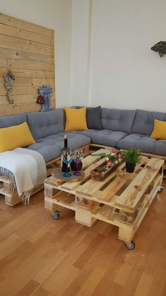 a living room with a stained accent wall, a pallet corner sofa, a pallet coffee table and some decor and pillows