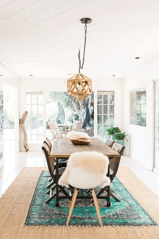 a lovely dining room with layered rugs, a jute rug and a colorful one, a stained table and mismatching chairs, and a pendant lamp