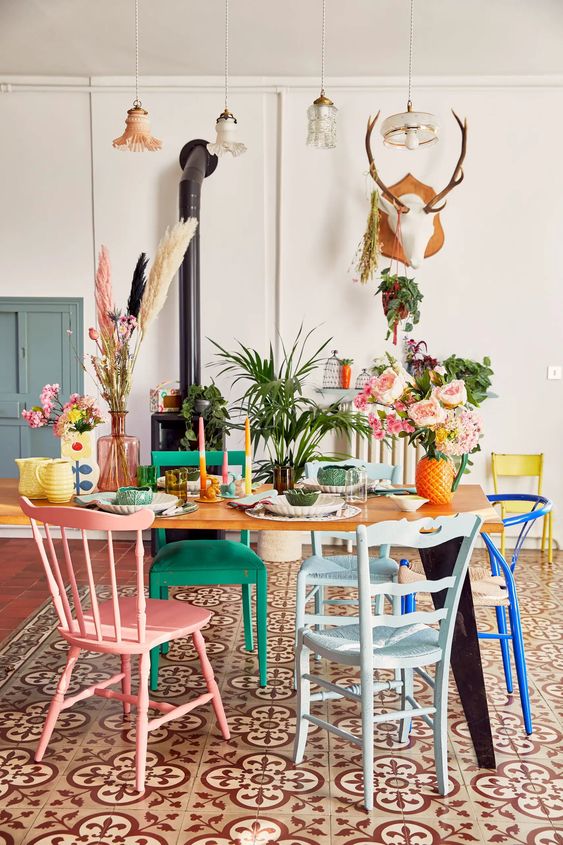 a maximalist dining room with a black hearth, a table, mismatching colorful chairs and bold decor